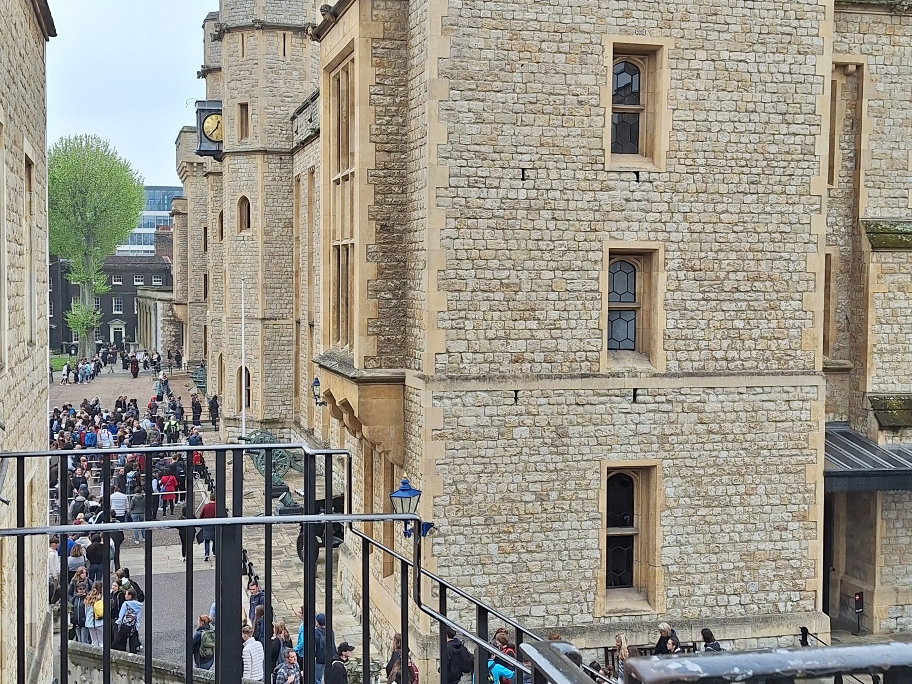 View from an elevated walkway inside the Tower of London showing stairs, railings, and uneven stone levels below